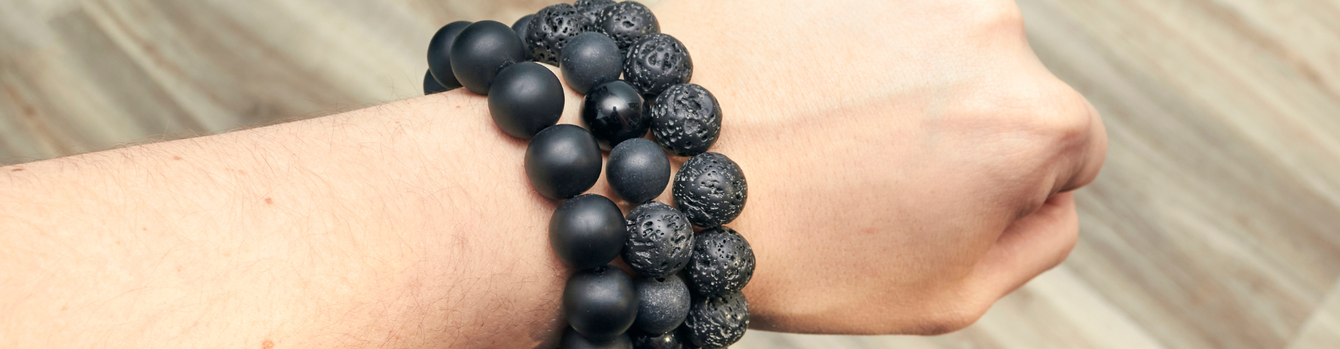 three black shungit lava bracelets on the background of a wooden floor are dressed on a hand