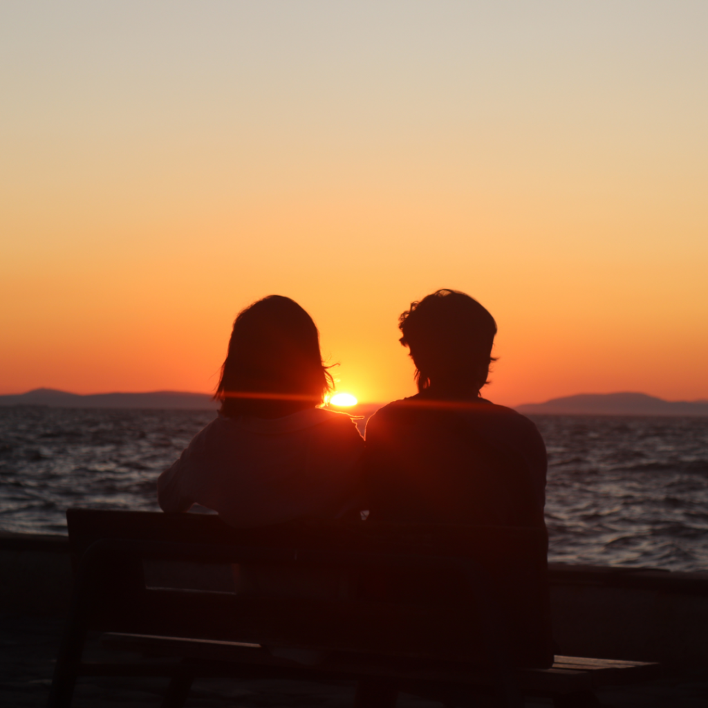 Silhouette of a Couple Sitting on Bench in Front of the Sea during Sunset